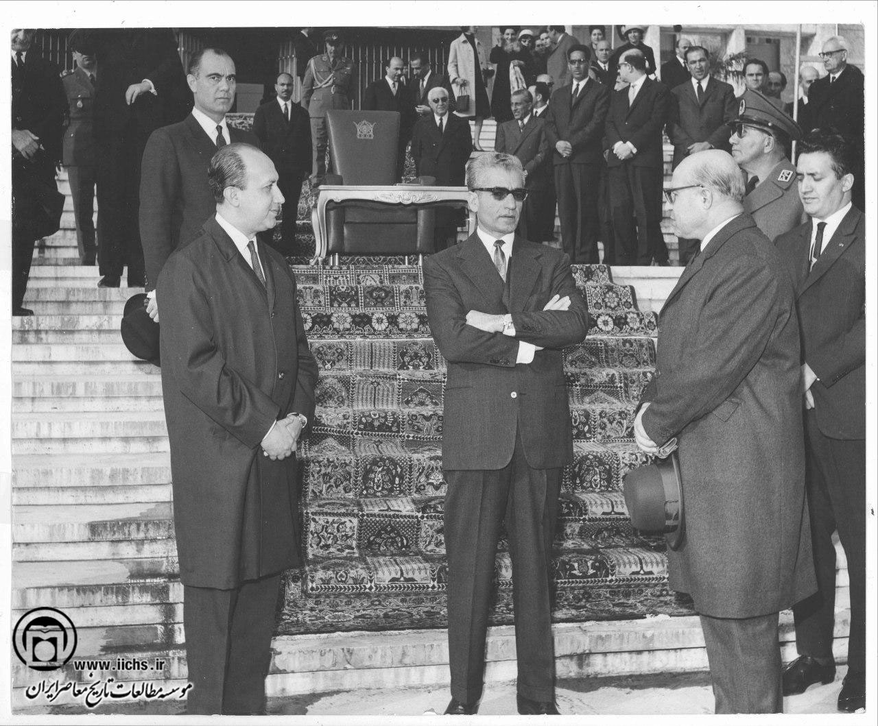 محمدرضا پهلوی به اتفاق حسنعلی منصور، نخست‌وزیر، و تنی چند از مقامات دولتی هنگام شرکت در یک مراسم در مقابل عمارت مجلس سنا