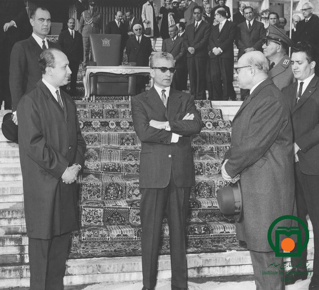 محمدرضا پهلوی به اتفاق حسنعلی منصور، نخست‌وزیر، و تنی چند از مقامات دولتی هنگام شرکت در یک مراسم در مقابل عمارت مجلس سنا